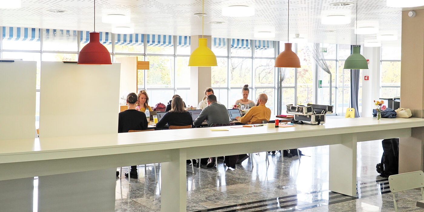 Ein Team arbeitet an der langen Tafel im RegioFood Hub, darüber farbige Hängelampen.